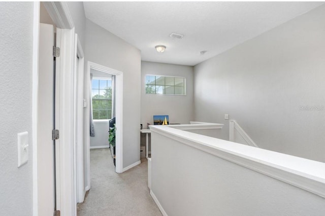 hall with light colored carpet, visible vents, baseboards, and an upstairs landing