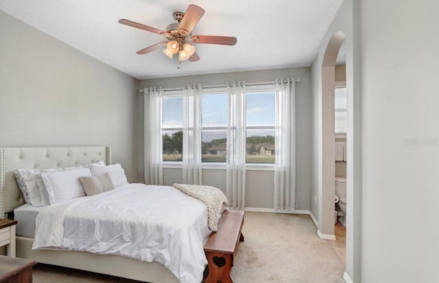 bedroom featuring arched walkways, a ceiling fan, baseboards, and light carpet