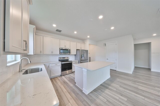 36959 Highland Meadows Ct, Zephyrhills, FL 33542 - kitchen with stainless steel appliances, a sink, a kitchen island, backsplash, and light wood-style flooring