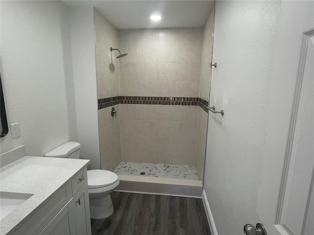 full bath with wood finished floors, a tile shower, toilet, and vanity