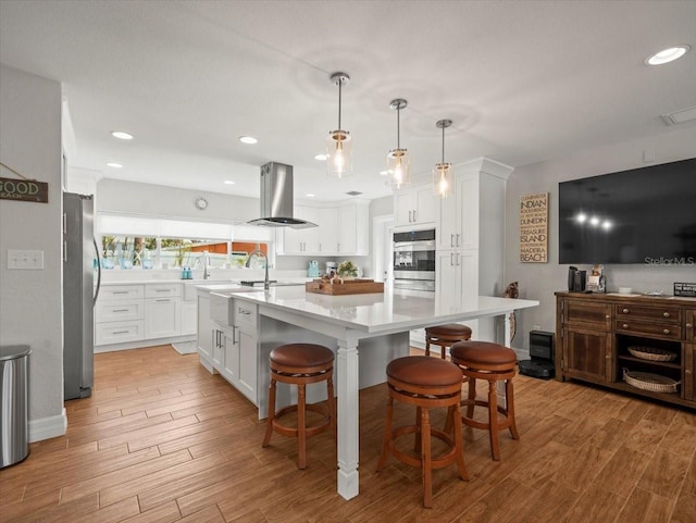 kitchen with light wood-type flooring, light countertops, appliances with stainless steel finishes, and island range hood
