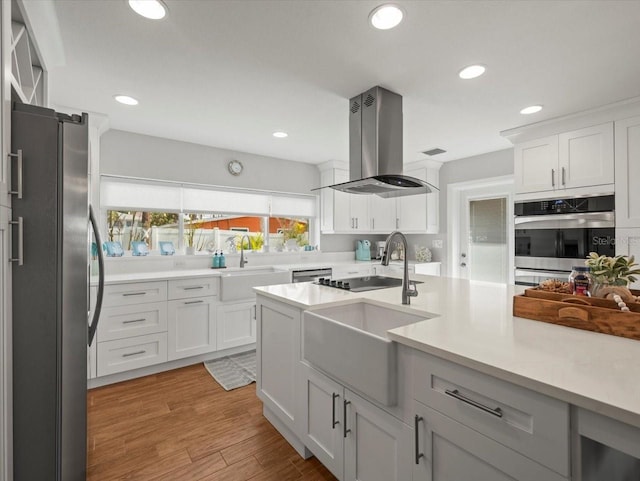 kitchen featuring a sink, recessed lighting, island range hood, light countertops, and appliances with stainless steel finishes