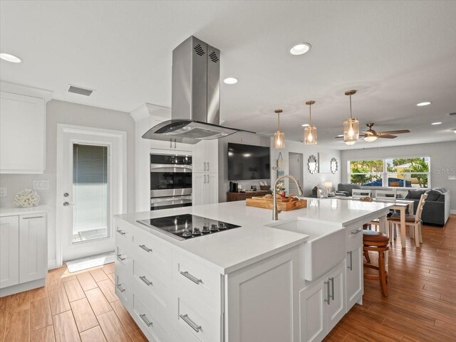 kitchen with recessed lighting, a sink, island exhaust hood, open floor plan, and black electric stovetop