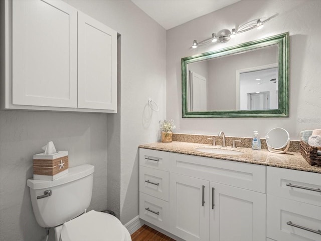 half bathroom featuring toilet, baseboards, vanity, and wood finished floors