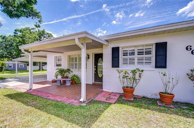 property entrance featuring stucco siding, a yard, and an attached carport