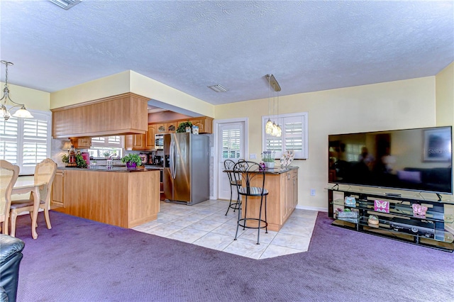 kitchen with appliances with stainless steel finishes, light colored carpet, dark countertops, a peninsula, and a notable chandelier