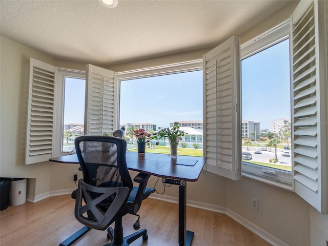 office featuring a textured ceiling, wood finished floors, a healthy amount of sunlight, and baseboards