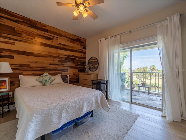 bedroom with light wood-style flooring, ceiling fan, access to outside, and wood walls