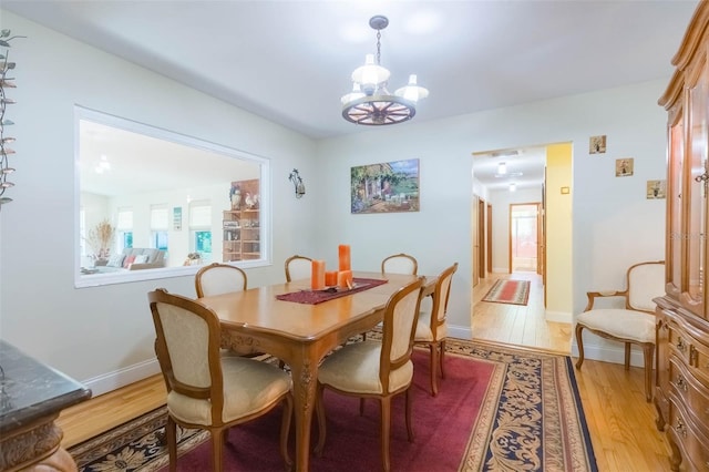 dining area featuring baseboards, light wood finished floors, and a notable chandelier