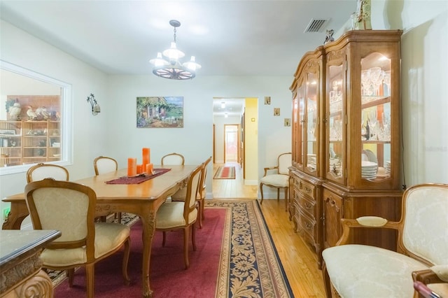 dining area featuring visible vents, light wood-style flooring, and an inviting chandelier