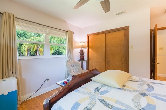 bedroom with visible vents, a closet, wood finished floors, baseboards, and a ceiling fan