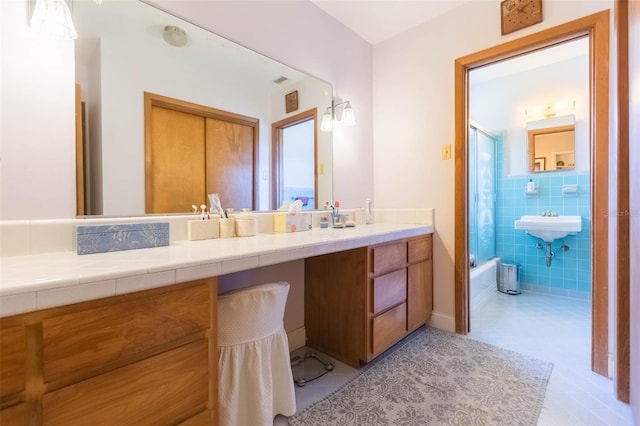 bathroom featuring vanity, enclosed tub / shower combo, tile patterned flooring, and tile walls