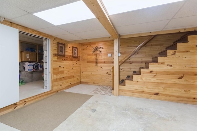 finished below grade area with a paneled ceiling, stairs, and wooden walls