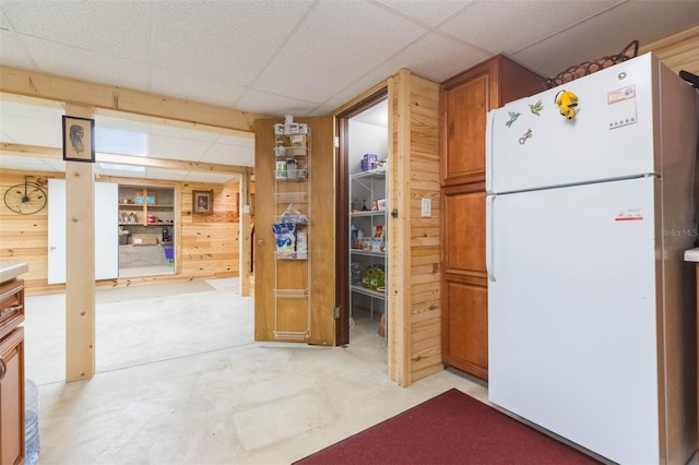 kitchen featuring freestanding refrigerator, concrete flooring, wood walls, and a paneled ceiling