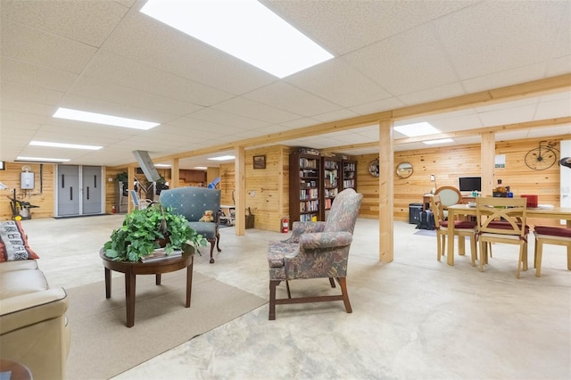living room featuring wood walls, concrete flooring, and a drop ceiling