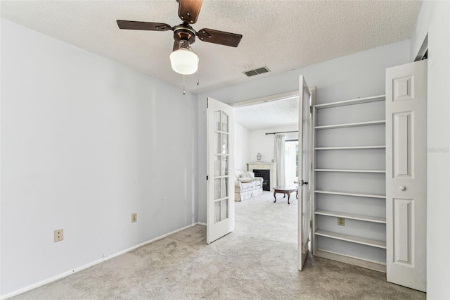 unfurnished bedroom featuring a tile fireplace, carpet flooring, visible vents, a textured ceiling, and french doors