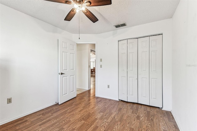 unfurnished bedroom featuring a textured ceiling, visible vents, wood finished floors, and baseboards
