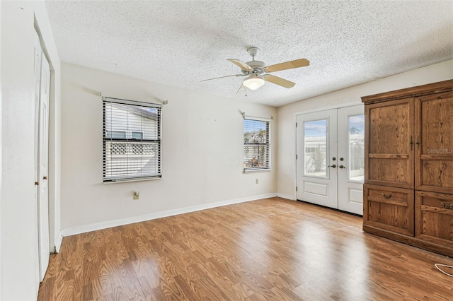 interior space featuring ceiling fan, light wood-style flooring, baseboards, a textured ceiling, and french doors