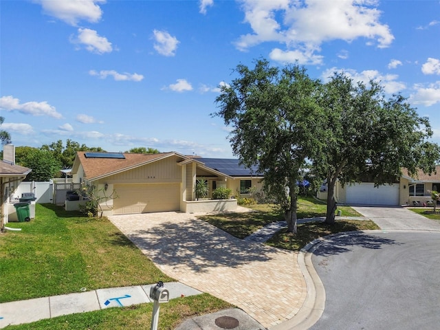 ranch-style house with a garage, roof mounted solar panels, driveway, and a front yard