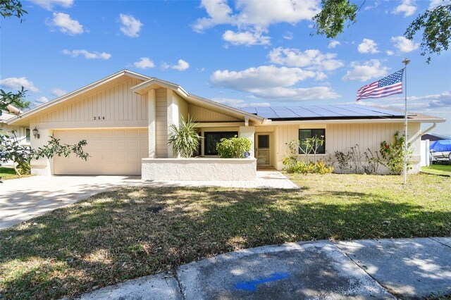 view of front of property featuring roof mounted solar panels, a front lawn, driveway, and an attached garage