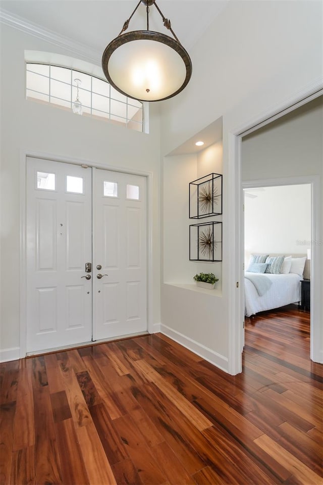 foyer featuring a towering ceiling, wood finished floors, ornamental molding, and baseboards