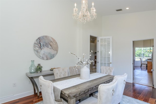 dining room with baseboards, wood finished floors, a notable chandelier, and a towering ceiling