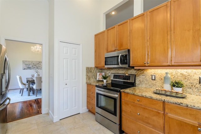 kitchen featuring tasteful backsplash, an inviting chandelier, light stone counters, stainless steel appliances, and a high ceiling