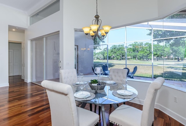dining area featuring an inviting chandelier, a towering ceiling, wood finished floors, and baseboards