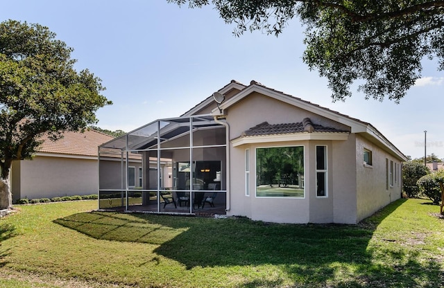 rear view of property featuring a lanai, stucco siding, a tile roof, and a lawn