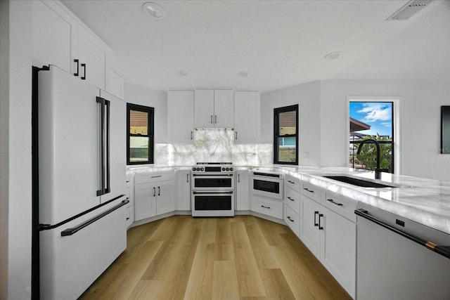 6627 Dolphin Cove Dr, Apollo Beach, FL 33572 - kitchen featuring premium appliances, light wood-type flooring, white cabinetry, backsplash, and light stone counters