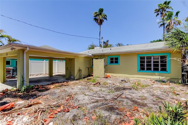 rear view of property with stucco siding, fence, and a carport