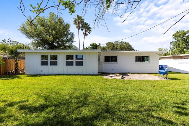 back of property with fence, board and batten siding, a yard, and a patio area