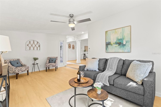 living area with ornate columns, light wood-type flooring, a ceiling fan, and baseboards