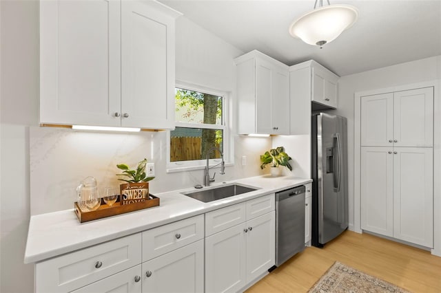 kitchen with white cabinetry, light wood-style flooring, a sink, appliances with stainless steel finishes, and light countertops