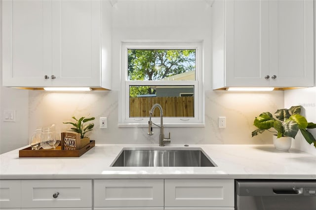 kitchen featuring stainless steel dishwasher, backsplash, a sink, and white cabinetry