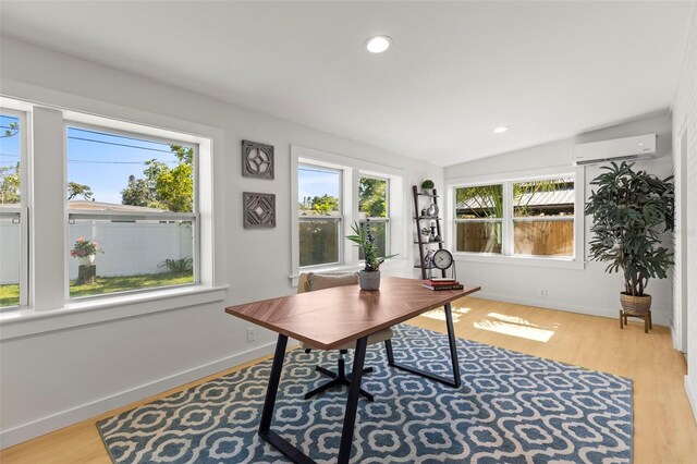 office area with wood finished floors, a wall unit AC, vaulted ceiling, and baseboards
