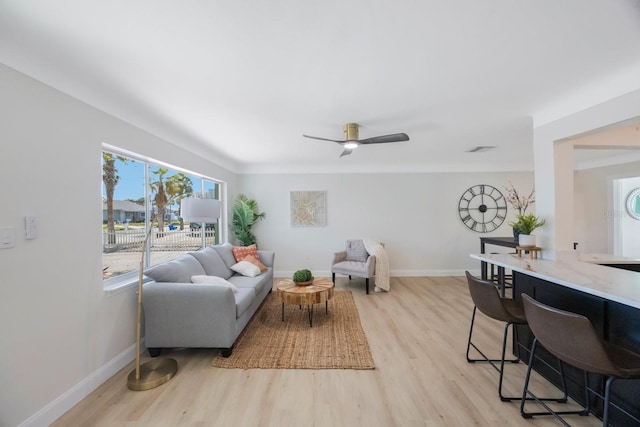 living area with ceiling fan, baseboards, visible vents, and light wood finished floors