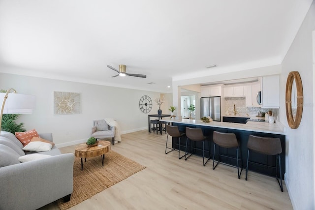 living area featuring light wood finished floors, a ceiling fan, and baseboards