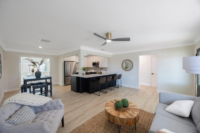 living room featuring light wood finished floors, visible vents, a ceiling fan, and baseboards