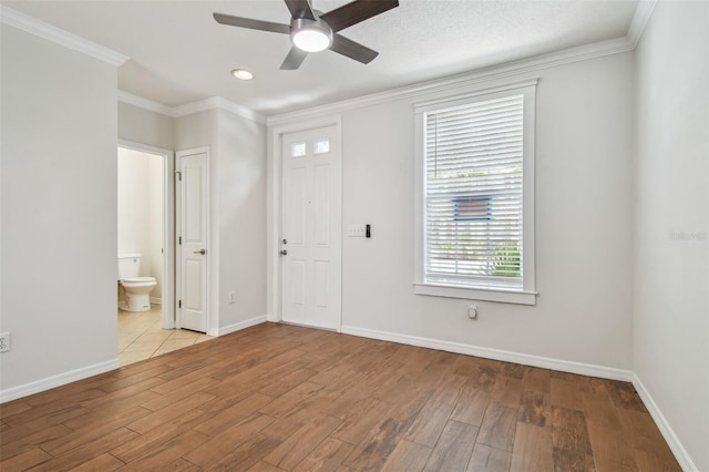 unfurnished bedroom featuring crown molding, baseboards, wood finished floors, and ensuite bathroom