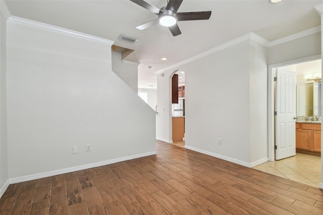 interior space featuring ornamental molding, baseboards, ceiling fan, arched walkways, and light wood-style flooring