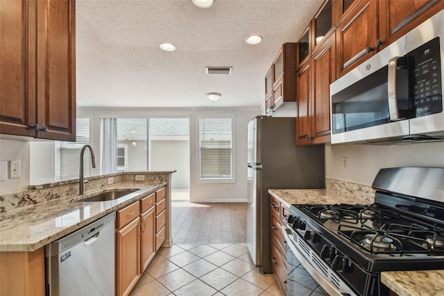 kitchen with light stone counters, a sink, a textured ceiling, stainless steel appliances, and light tile patterned floors
