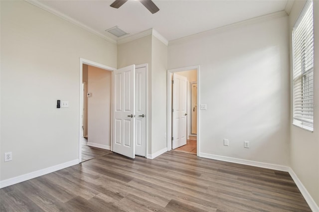 unfurnished bedroom with baseboards, ornamental molding, wood finished floors, and multiple windows