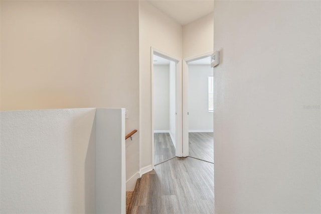 hallway featuring baseboards, wood finished floors, and an upstairs landing