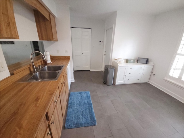 kitchen with a sink, baseboards, and wood counters