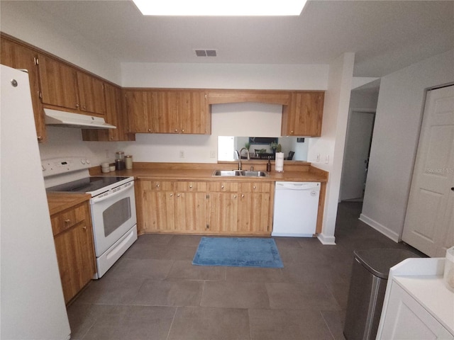 kitchen featuring visible vents, white appliances, under cabinet range hood, dark tile patterned flooring, and a sink