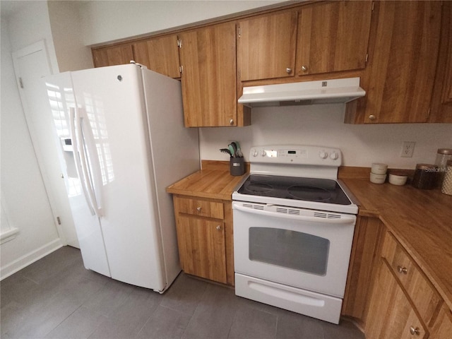 kitchen with white appliances, light countertops, brown cabinetry, under cabinet range hood, and dark tile patterned floors