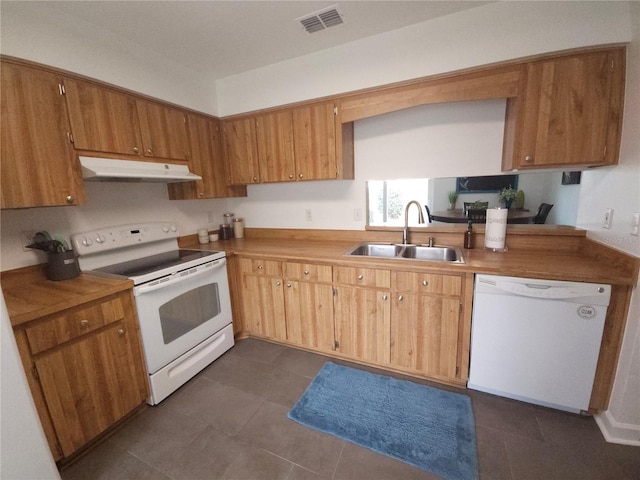 kitchen featuring visible vents, white appliances, under cabinet range hood, dark tile patterned flooring, and a sink