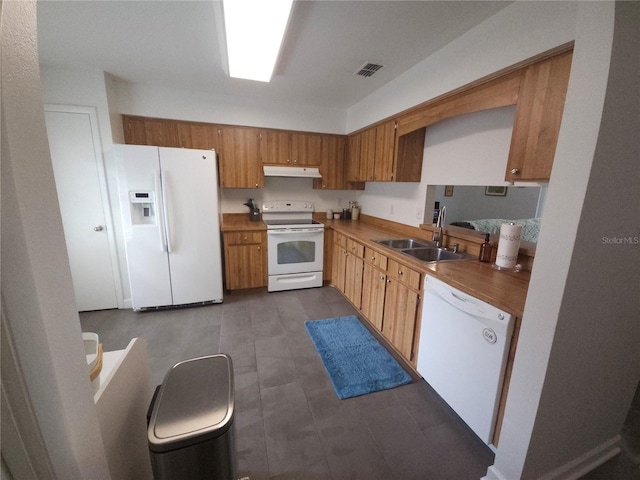 kitchen with a sink, white appliances, brown cabinetry, under cabinet range hood, and visible vents