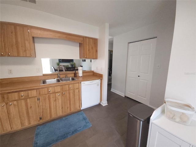 kitchen featuring brown cabinets, white dishwasher, a sink, light countertops, and washer / dryer